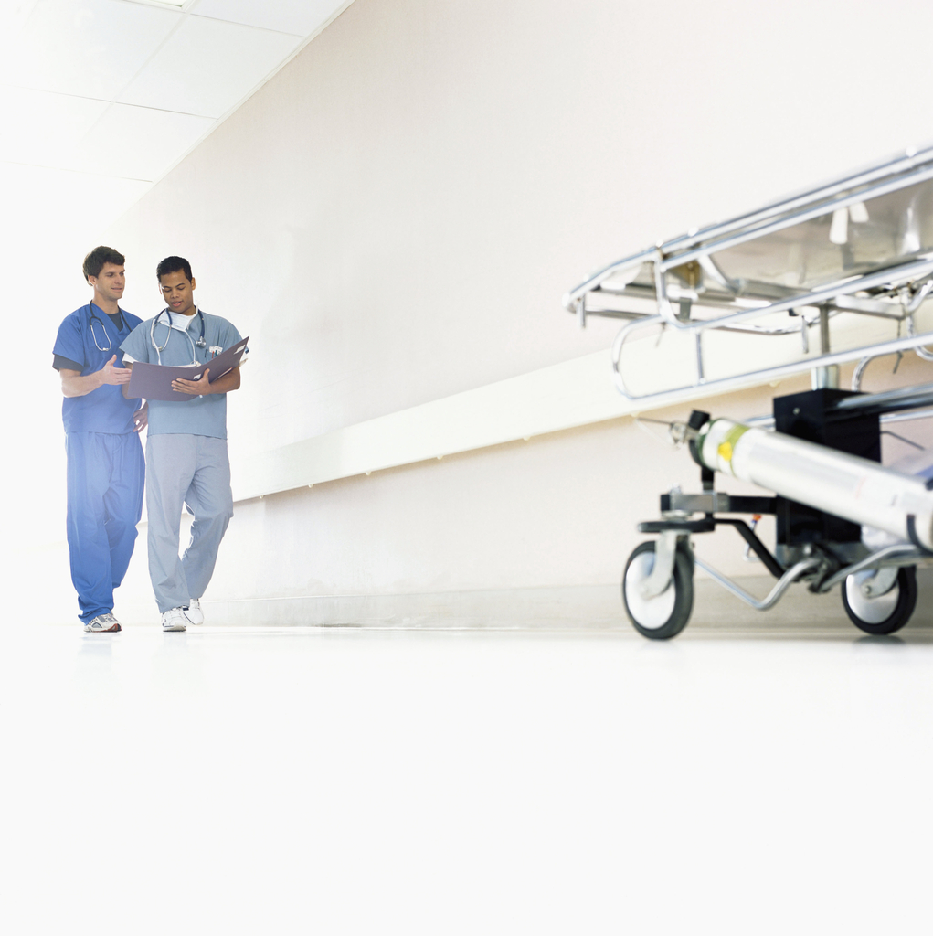 a nurse and doctor in scrubs walk down a hall while looking at medical chart
