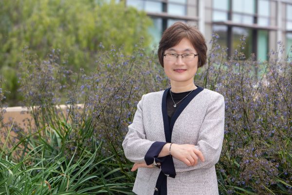 Photo of Jung-Ah Lee standing authoritatively in front of greenery